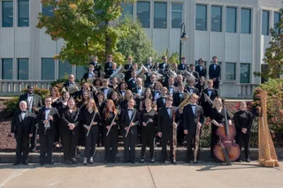 L'orchestre de l'Université de Virginie de l'Ouest posant pour une photo de groupe avec tous leurs instruments et en jolies tenues devant leur université.