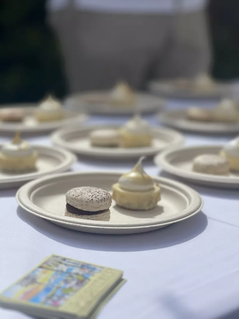 Sur une table avec une nappe blanche, des assiettes sont déposées avec chacune deux petits desserts à l'intérieur. Des cartes de visite sont déposées au devant