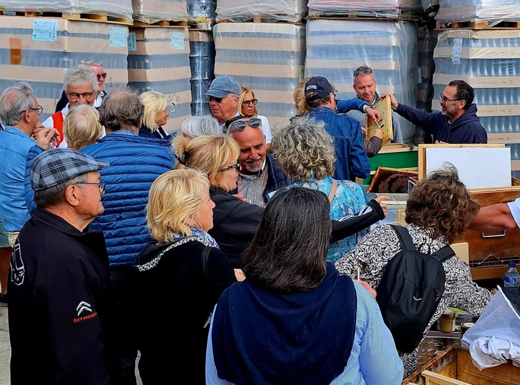 Découverte et explication du fonctionnement des ruches pour la fabrication du miel avec une foule intéressée au milieu d'un stock de bouteilles en verre