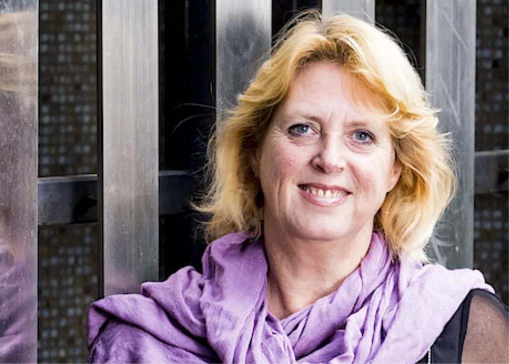 Miriam souriant face à la caméra, vêtue d'un châle rose et d'un chemisier noir