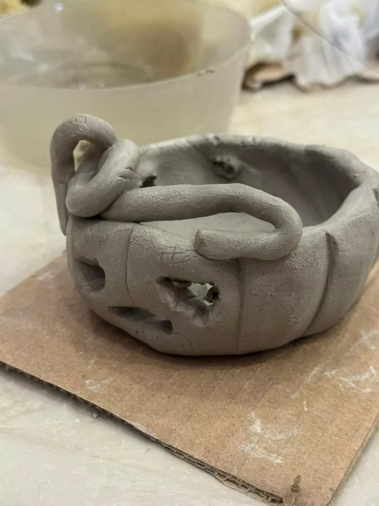 Création en argile d'un bol en forme de citrouille, posé sur un carton pour le laisser sécher.