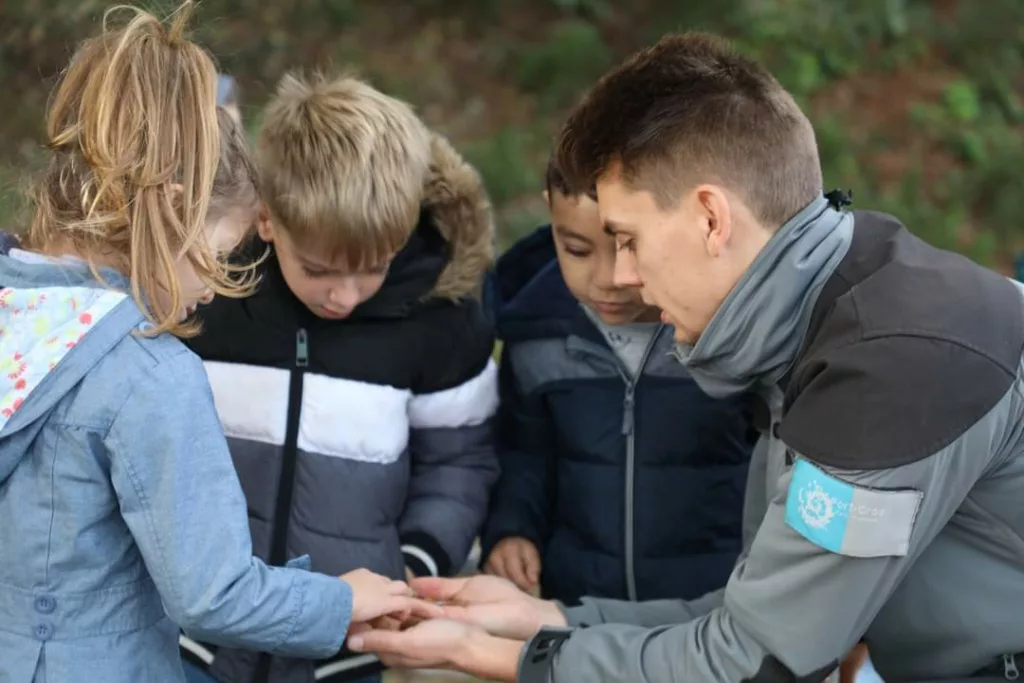 Un guide du Parc National de Port Cros est en train de montrer quelque chose dans le creux de sa main à trois jeunes enfants qui sont intrigués.