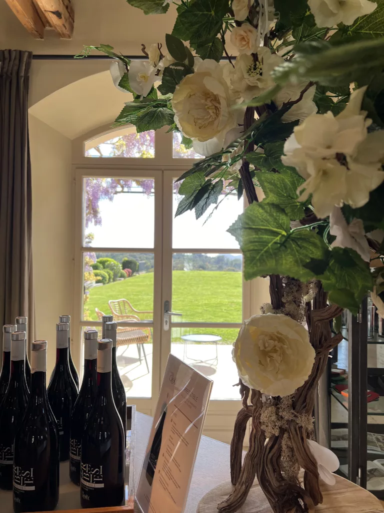 © lacroixvalmertourisme Intérieur du caveau du domaine de la croix avec des roses blanches et des bouteilles de leur vin rouge, le tout disposé devant une fenetre avec vue sur le jardin. Dehors il fait beau