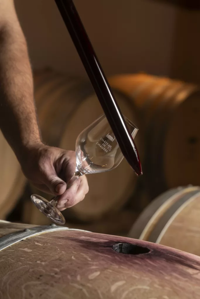 ©LHJ photo Le maître de chai est en train de gouter le vin rouge qui repose dans la barrique. Il a un verre à vin dans une main et un pipette en verre dans l'autre