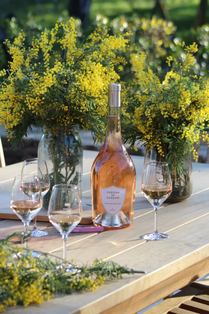 Magnum de rosé Château de Chausse ©Margot Inzirillo Bouteille de vin rosé au milieu de mimosas, sur une table avec des verres à vin pour un moment convivial en vacances